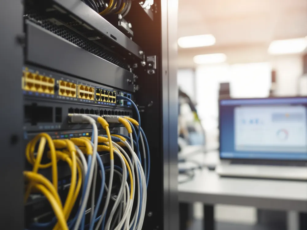 Szafa serwerowa z uporządkowanymi kablami sieciowymi i laptopem z panelem monitoringu w tle